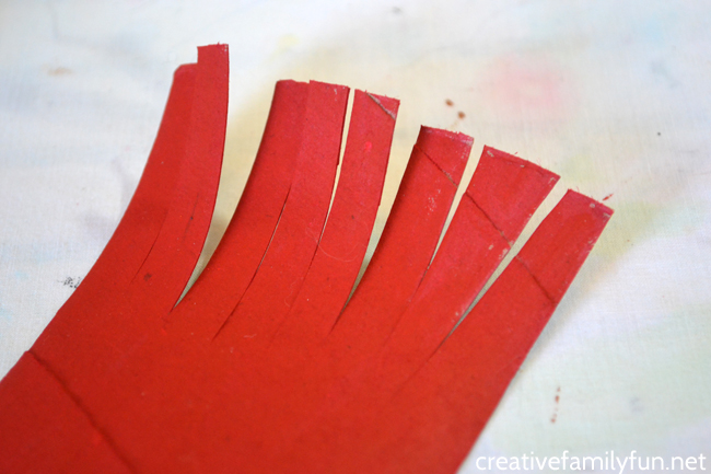 Close up of a piece of cardboard tube painted red with fringes cut at the top